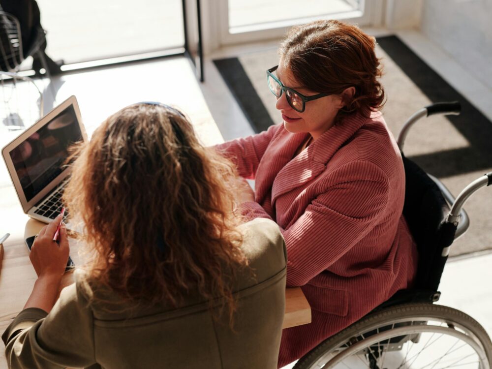 Woman in wheelchair and carer sat at desk with laptop